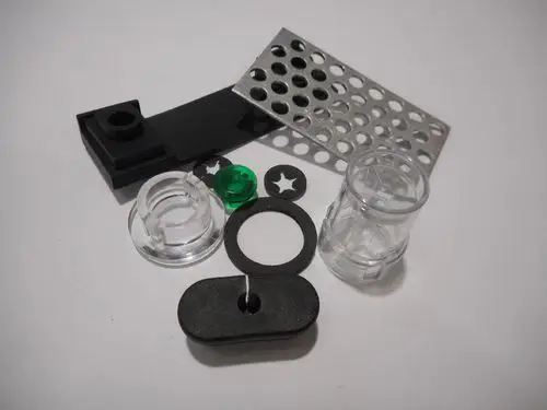 Set aus verschiedenen Kleinteilen von Remeha, bestehend aus transparenten und schwarzen Kunststoffkomponenten sowie einer Metallplatte mit Löchern.